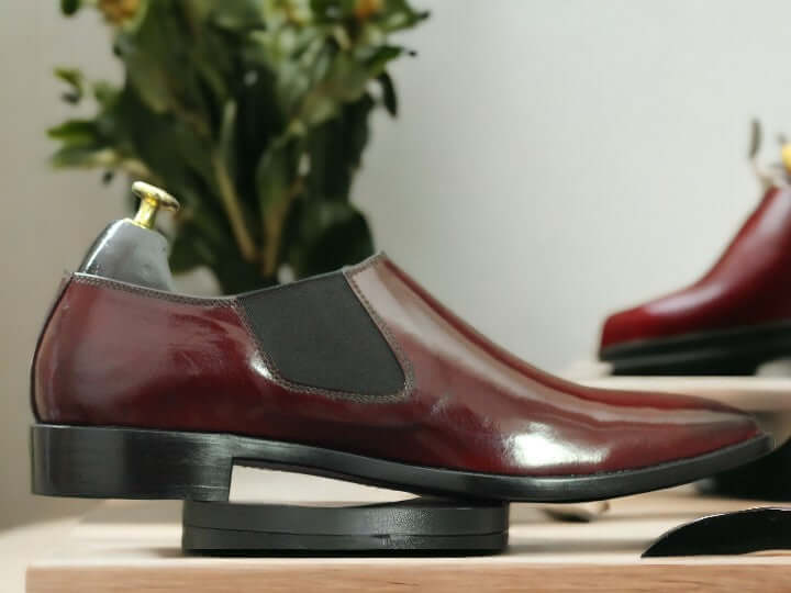 These Men's Maroon Patent Chelsea Shoes are handcrafted from high-quality leather, providing a polished and sophisticated look suitable for any dressy occasion. Featuring the classic Chelsea style with a sleek patent finish, these shoes are sure to elevate any outfit. Perfect for any fashion-forward man looking to make a statement.